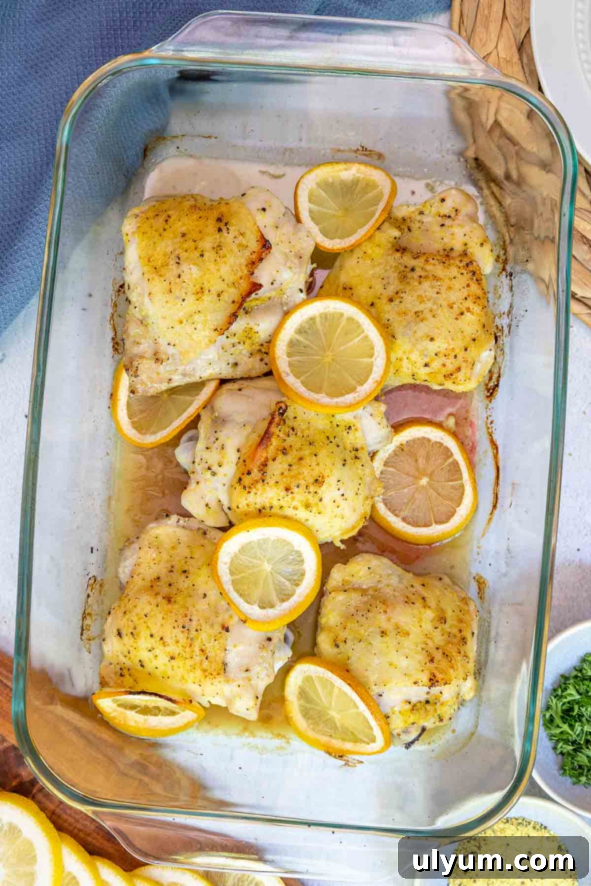 Golden Lemon Pepper Chicken Thighs 8 Cooked lemon pepper chicken thighs fresh out of the oven in a glass baking dish, surrounded by roasted lemon slices and pan juices.