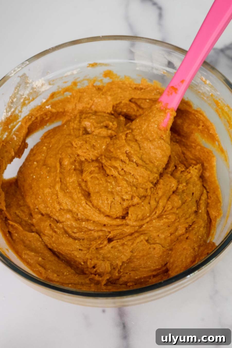 Pumpkin Spice Cake Loaf 5 A glass mixing bowl filled with thick, pumpkin bread batter being stirred with a silicone spatula.