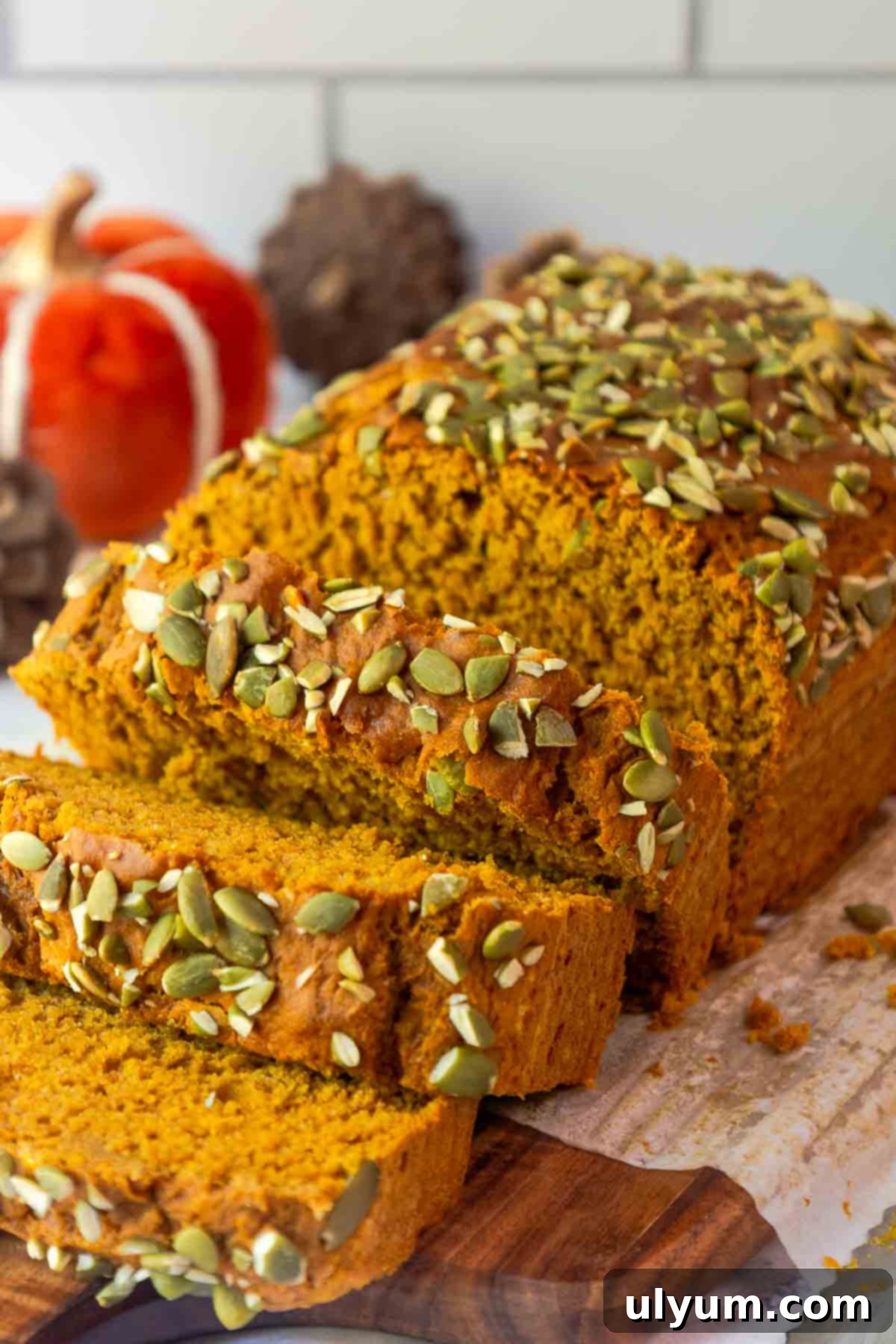 Pumpkin Spice Cake Loaf 9 Pumpkin bread partially sliced on a cutting board, showing its tender crumb and topping of green pepitas.