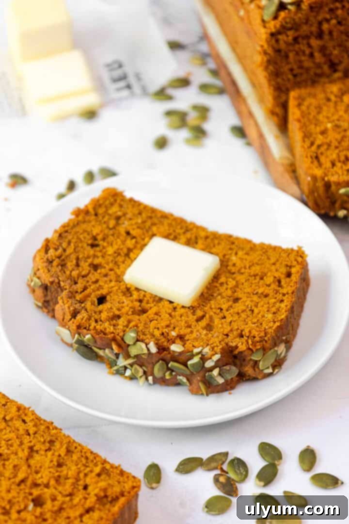 Pumpkin Spice Cake Loaf 10 A single slice of pumpkin bread on a white plate with a pat of butter melting on top.