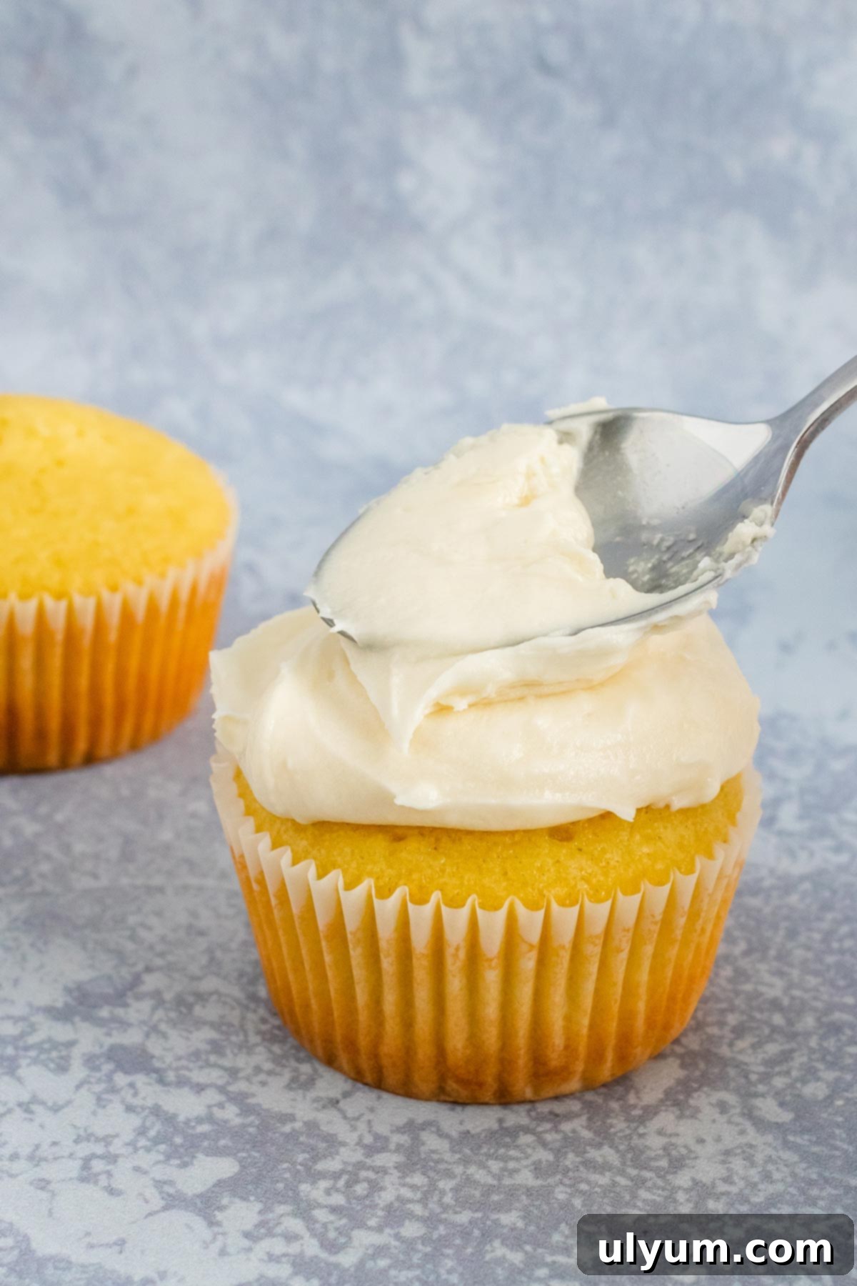 Velvet American Buttercream 3 A hand frosting a cupcake with creamy buttercream using a spoon.