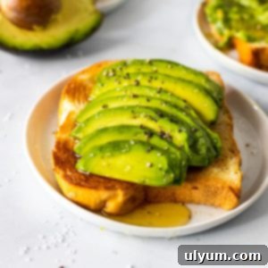A slice of toast topped with thick slices of avocado, sea salt, course black pepper, and a drizzle of honey