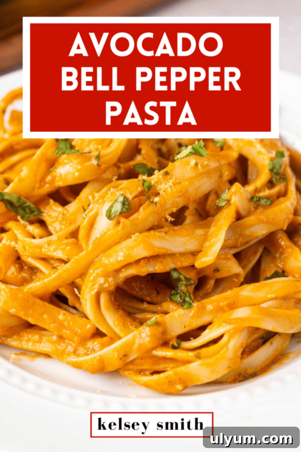 Avocado bell pepper pasta on a plate garnished with fresh basil. The image is overlayed with text saying 'Avocado Bell Pepper Pasta'.