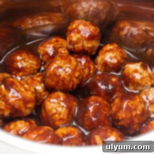 Instant Pot BBQ Meatballs in a silver Instant Pot liner, coated in a rich, glossy barbecue sauce, garnished with fresh herbs.