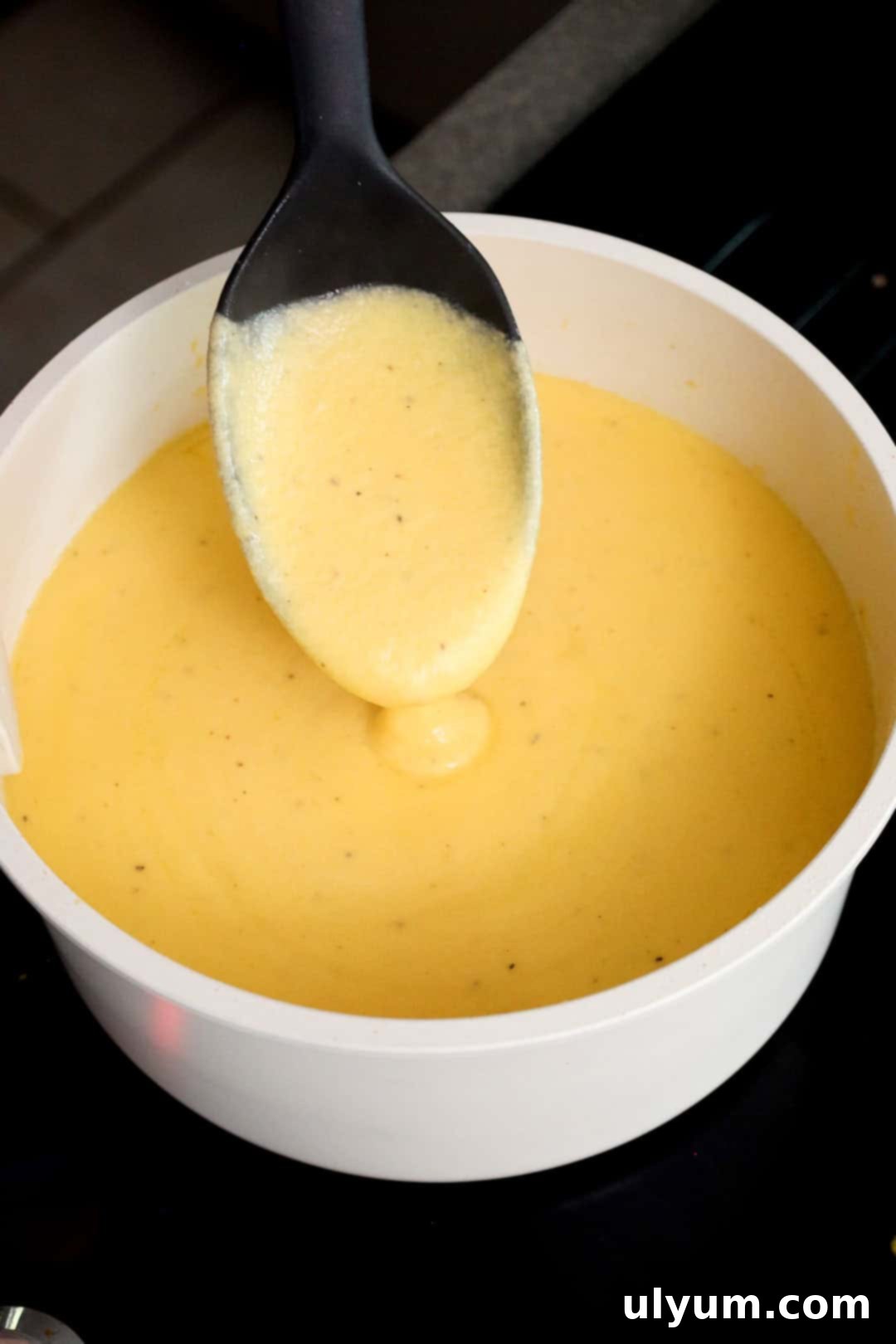 Thick, creamy cheese sauce made from shredded cheddar and milk being stirred with a spoon in a saucepan.