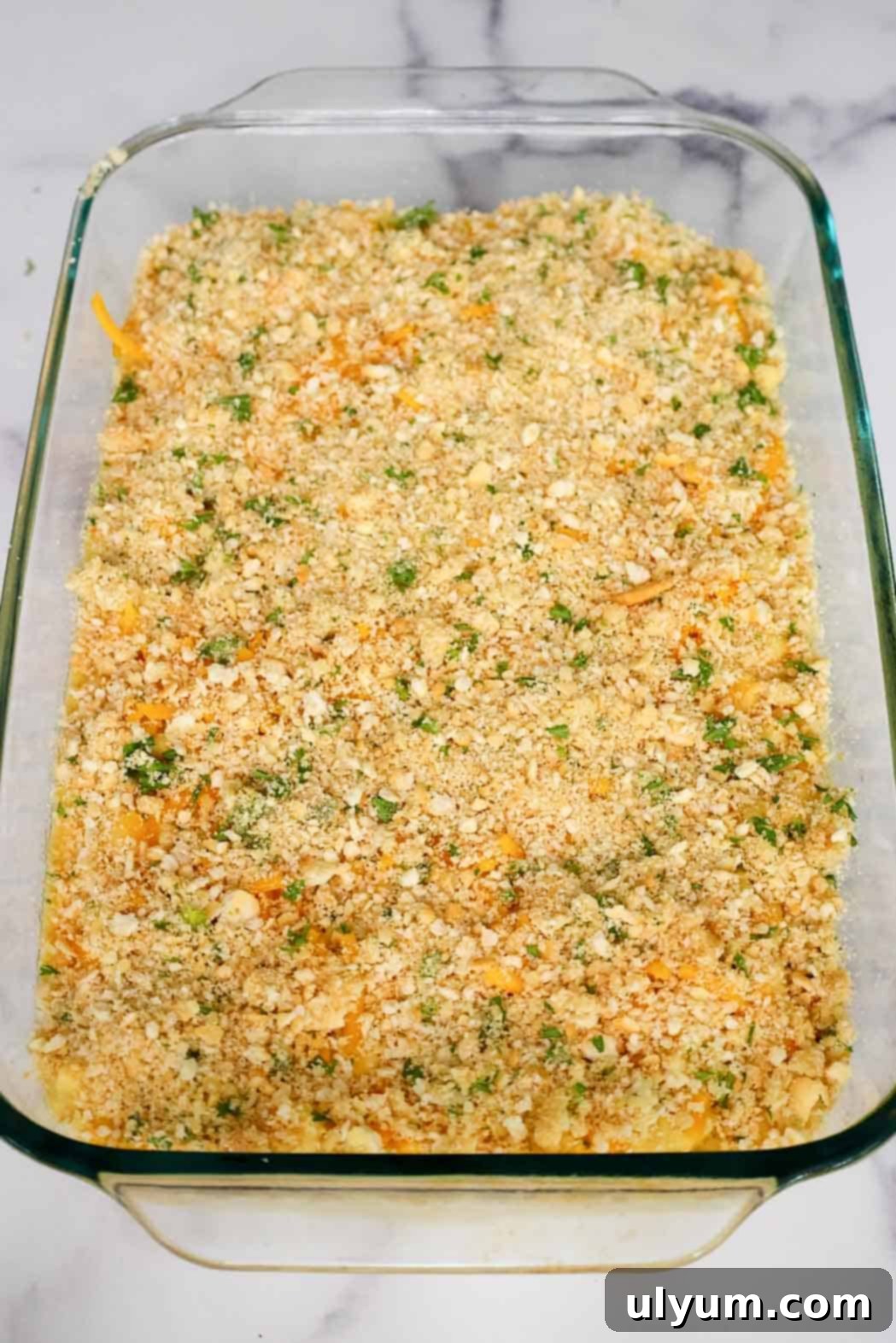 Casserole dish of mac and cheese fully layered with crushed Ritz crackers and parsley, prepped and ready for baking.