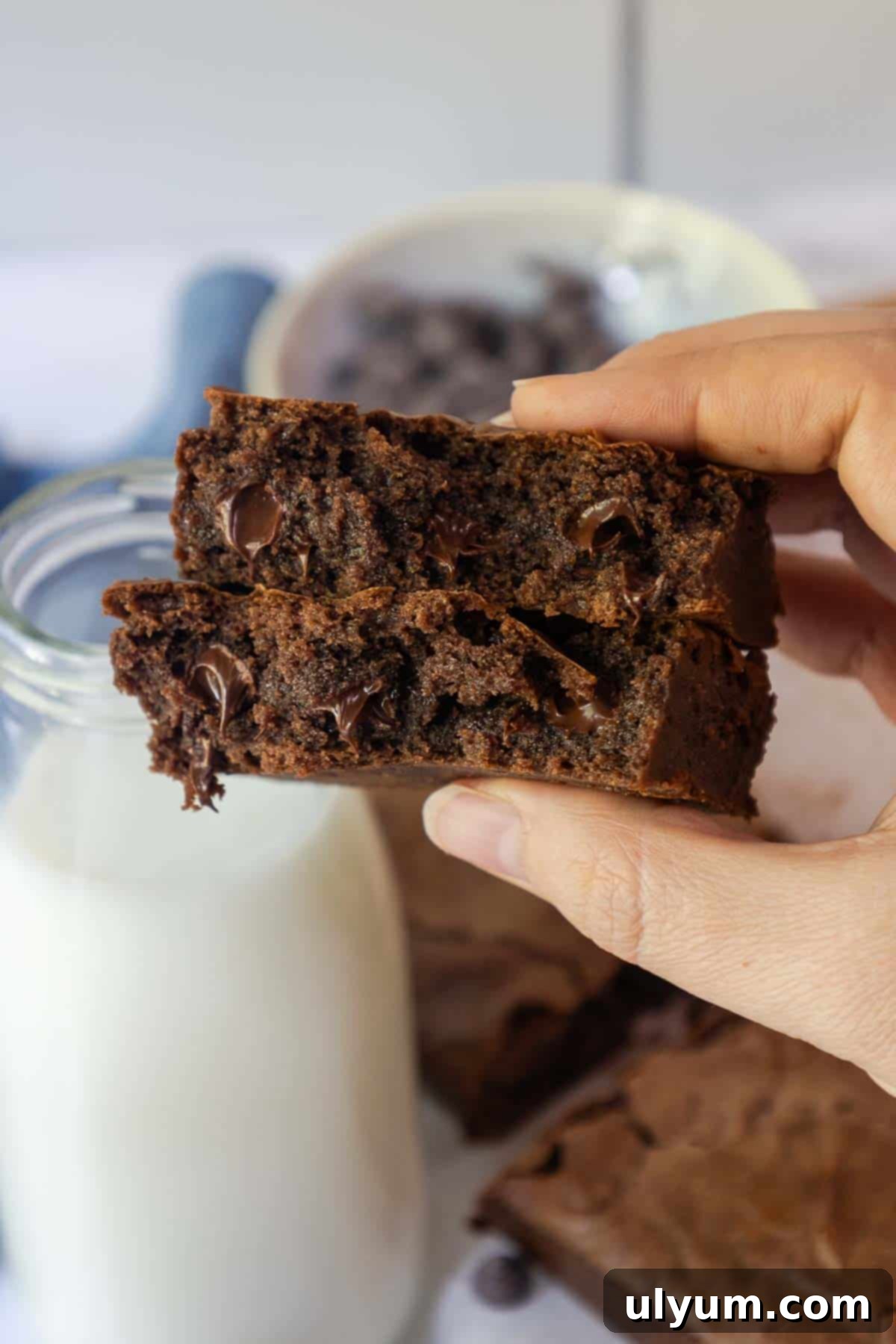 Hand holding two stacked brownies with melted chocolate chips visible inside.