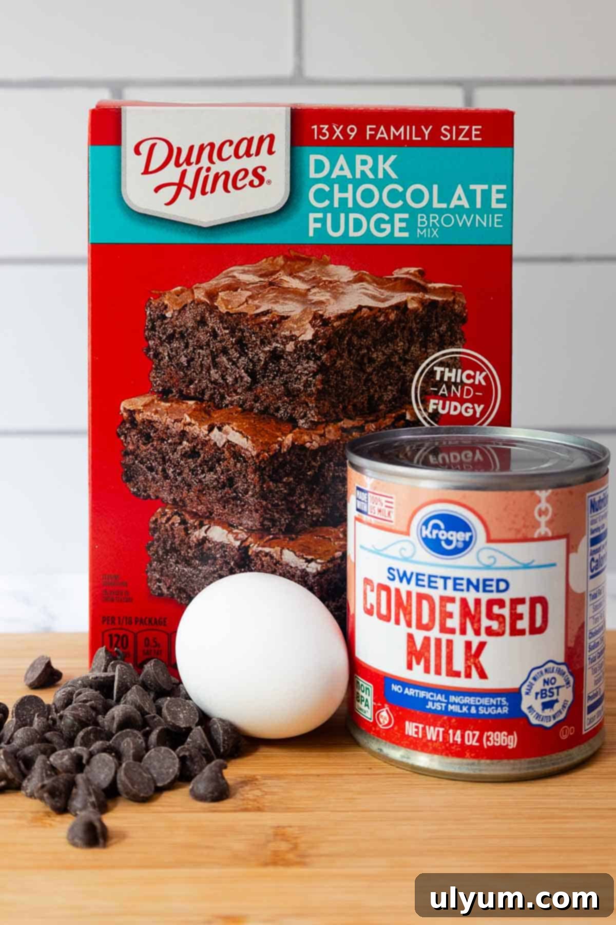 Box of Duncan Hines dark chocolate fudge brownie mix, a can of Kroger sweetened condensed milk, a white egg, and a pile of chocolate chips.