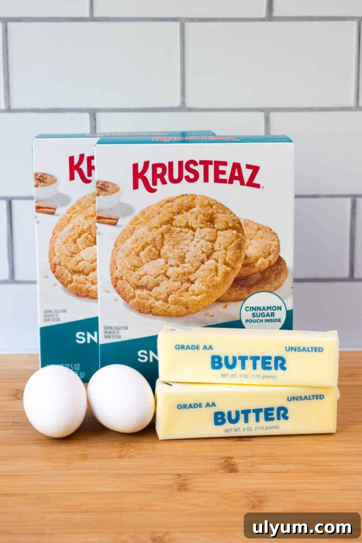 Two boxes of snickerdoodle cookie mix, two sticks of unsalted butter, and two eggs arranged on a cutting board.