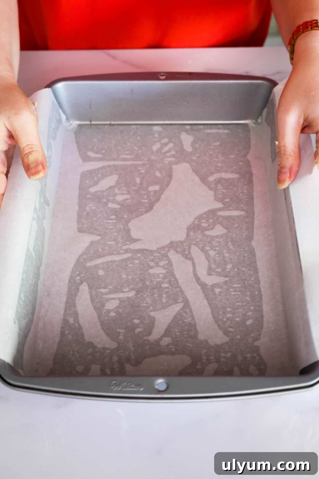 A parchment-lined metal baking pan being prepared by hand, ready to be filled with cookie dough.
