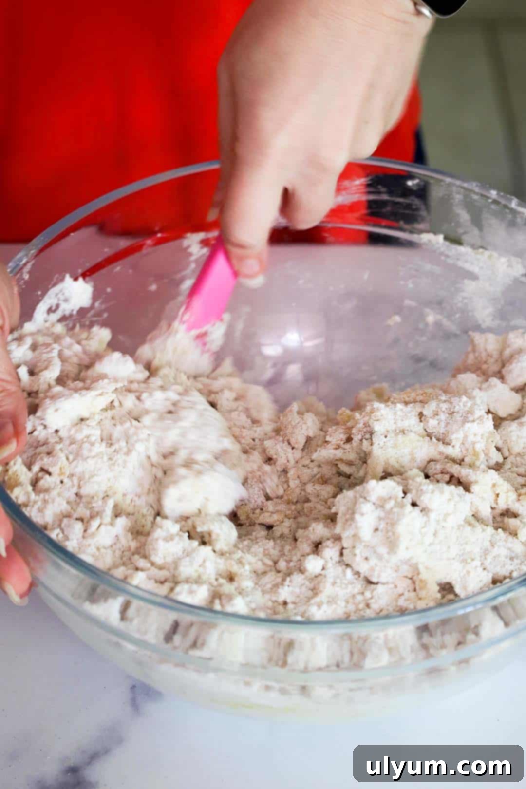 Cookie dough being mixed in a large mixing bowl until the dough has a shaggy texture.