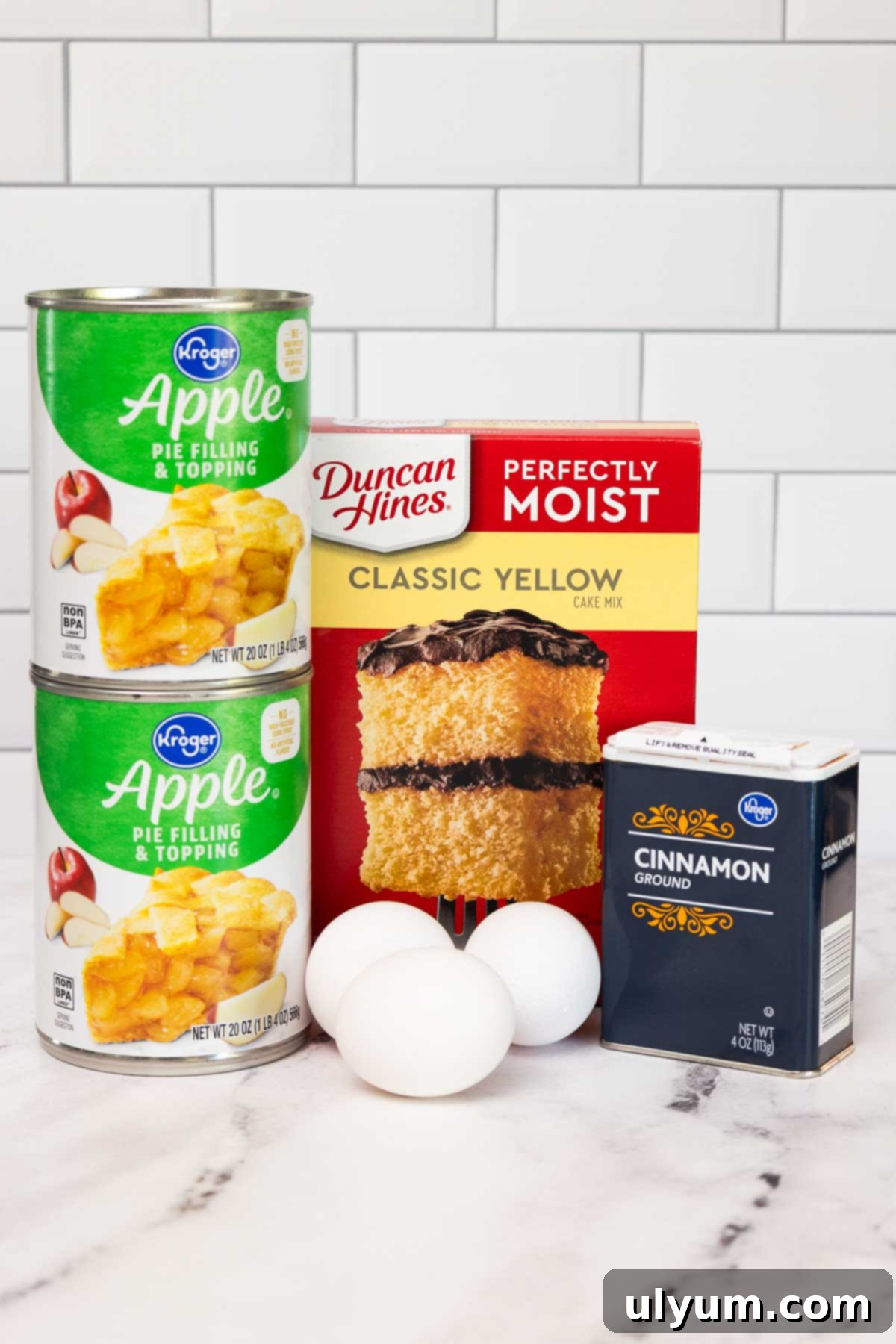 Ingredients for apple cake including canned apple pie filling, classic yellow cake mix, ground cinnamon, and three eggs.