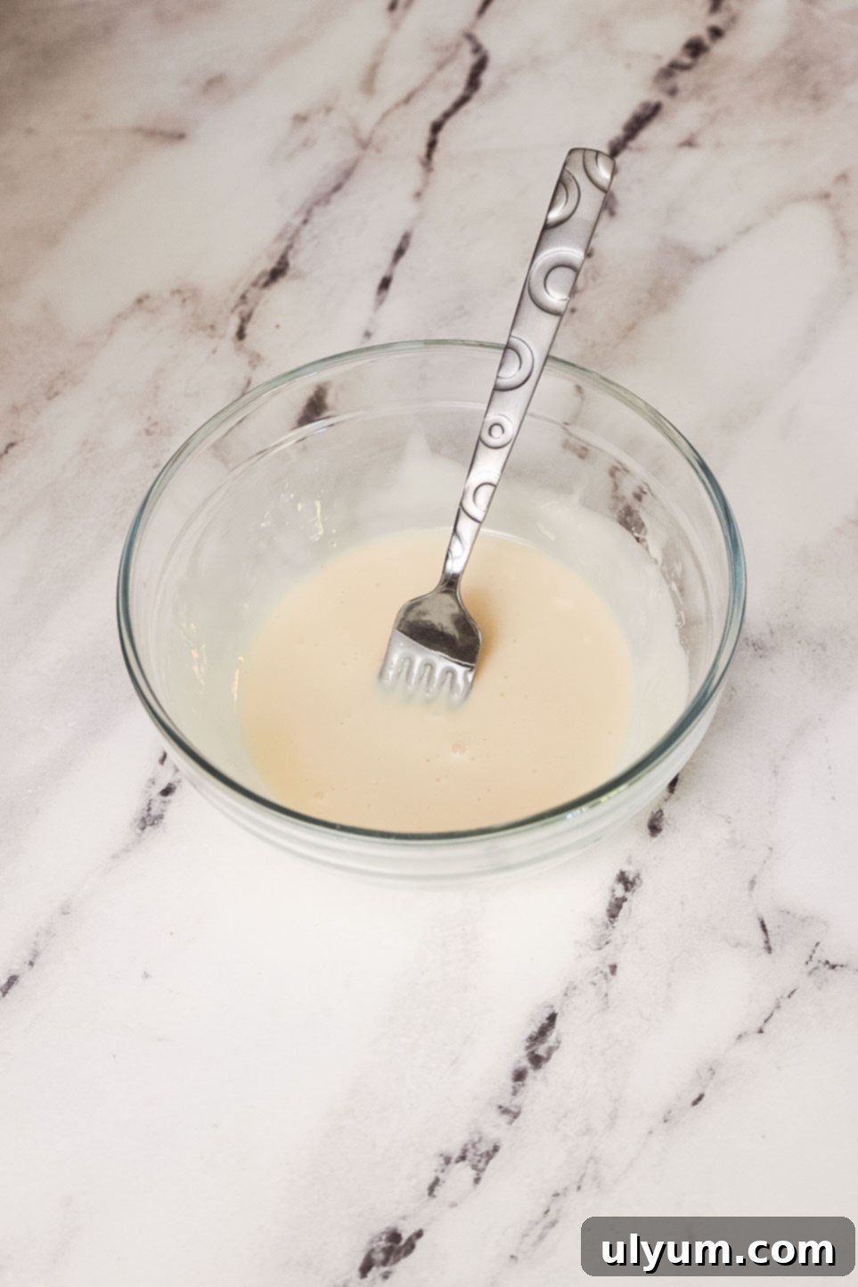 A small glass bowl of vanilla glaze with a fork.