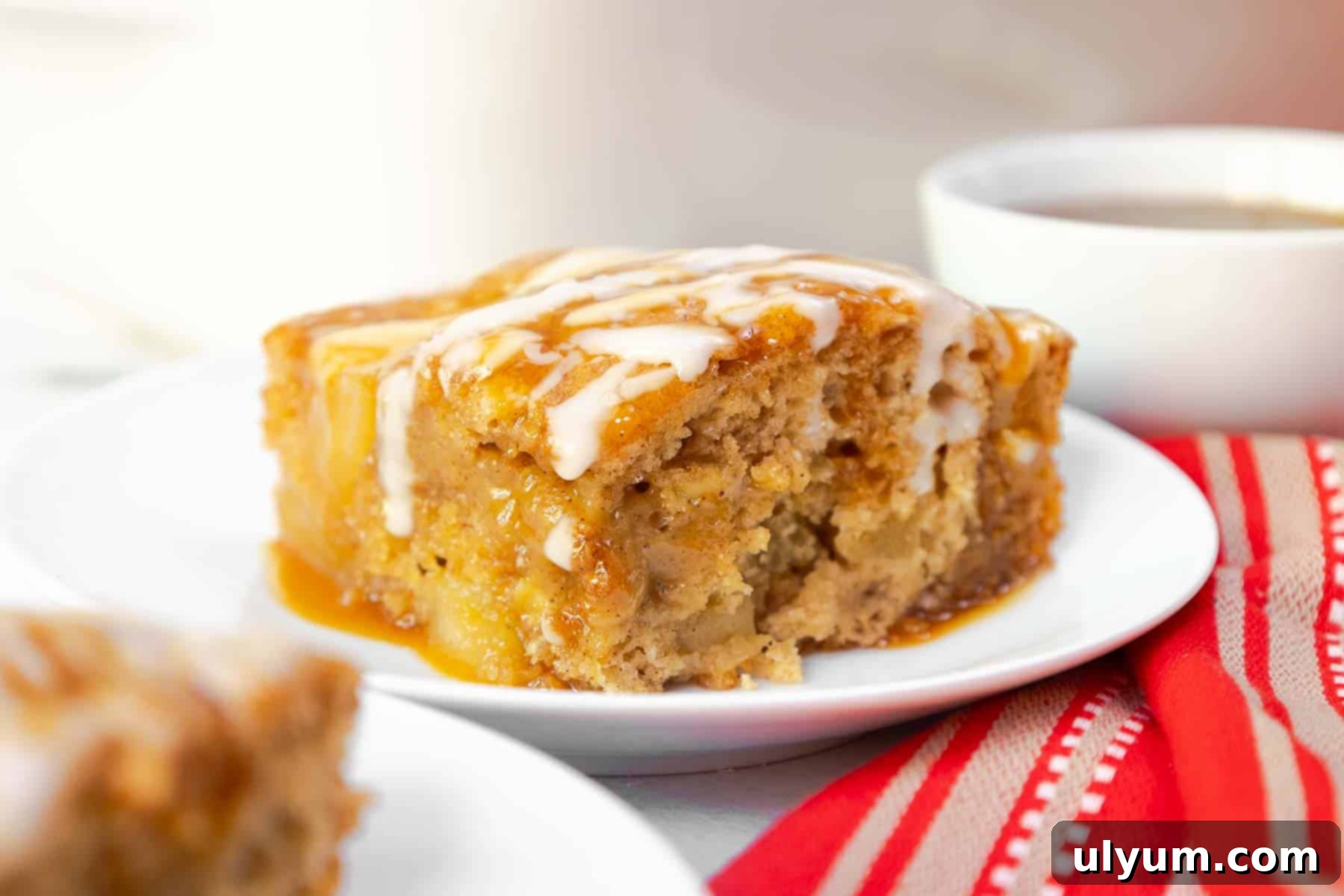 A generous slice of apple cake with visible apple chunks, topped with glaze and caramel.