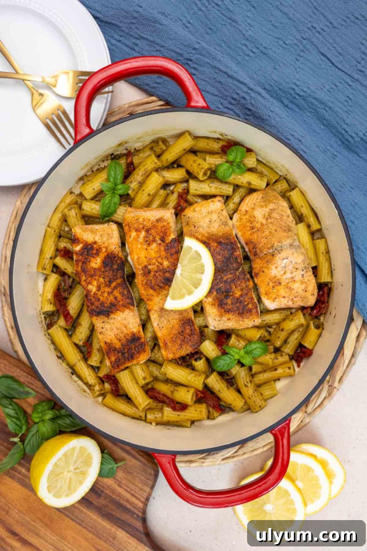 Top-down view of pot filled with salmon pesto pasta topped with four seared salmon fillet on top of rigatoni with sun-dried tomatoes.