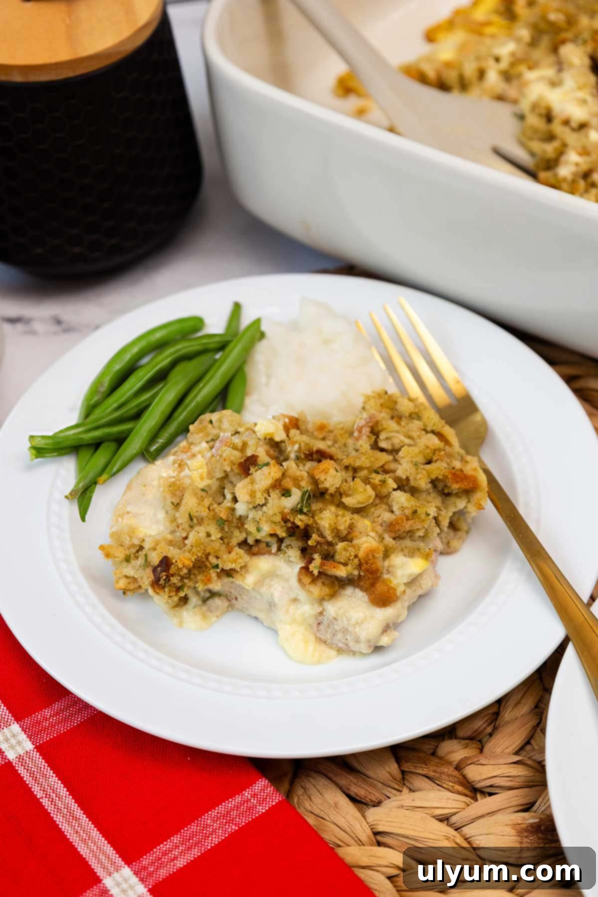 Baked pork chops with stuffing served on a white plate with green beans and mashed potatoes.