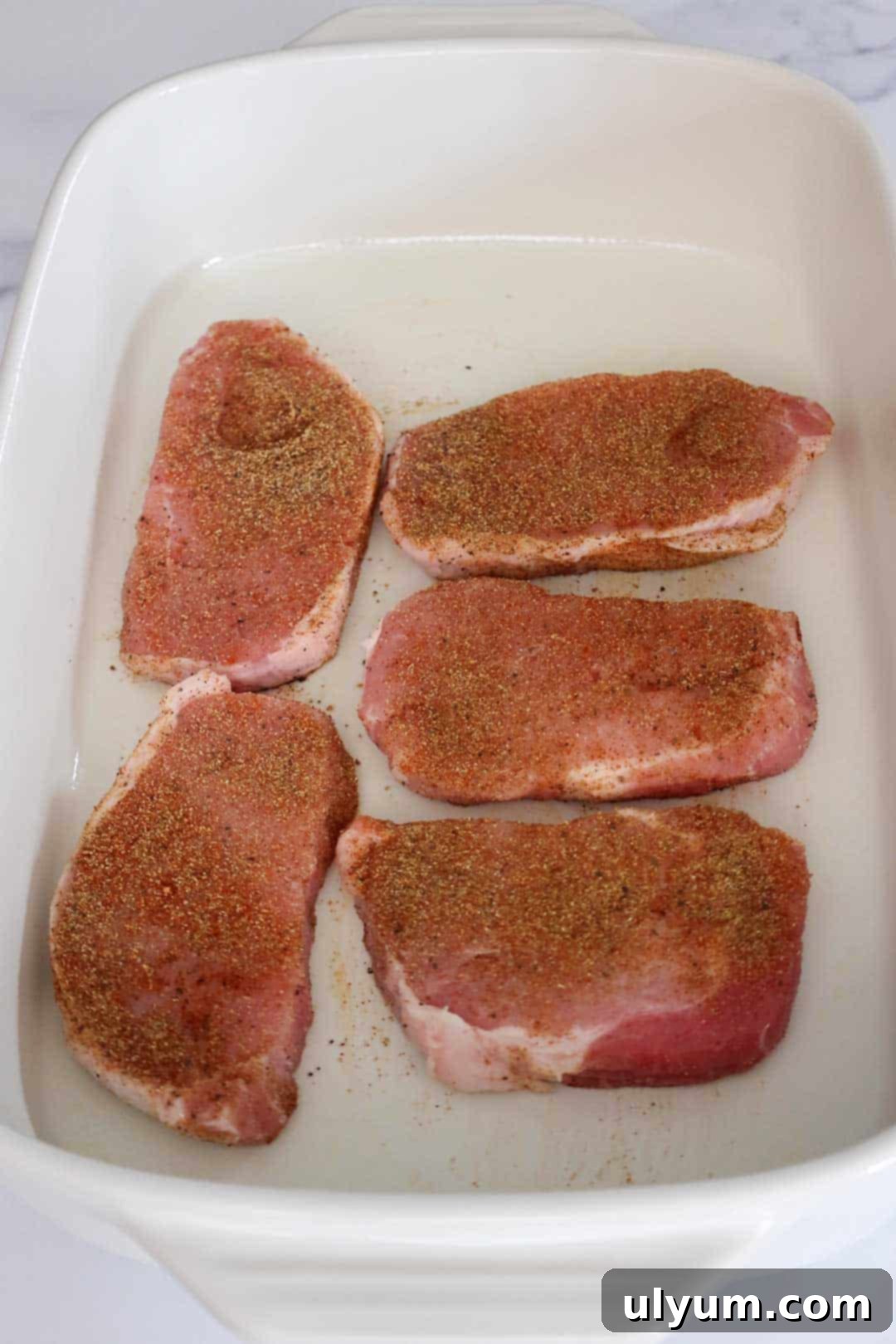 Seasoned raw pork chops in a baking dish.