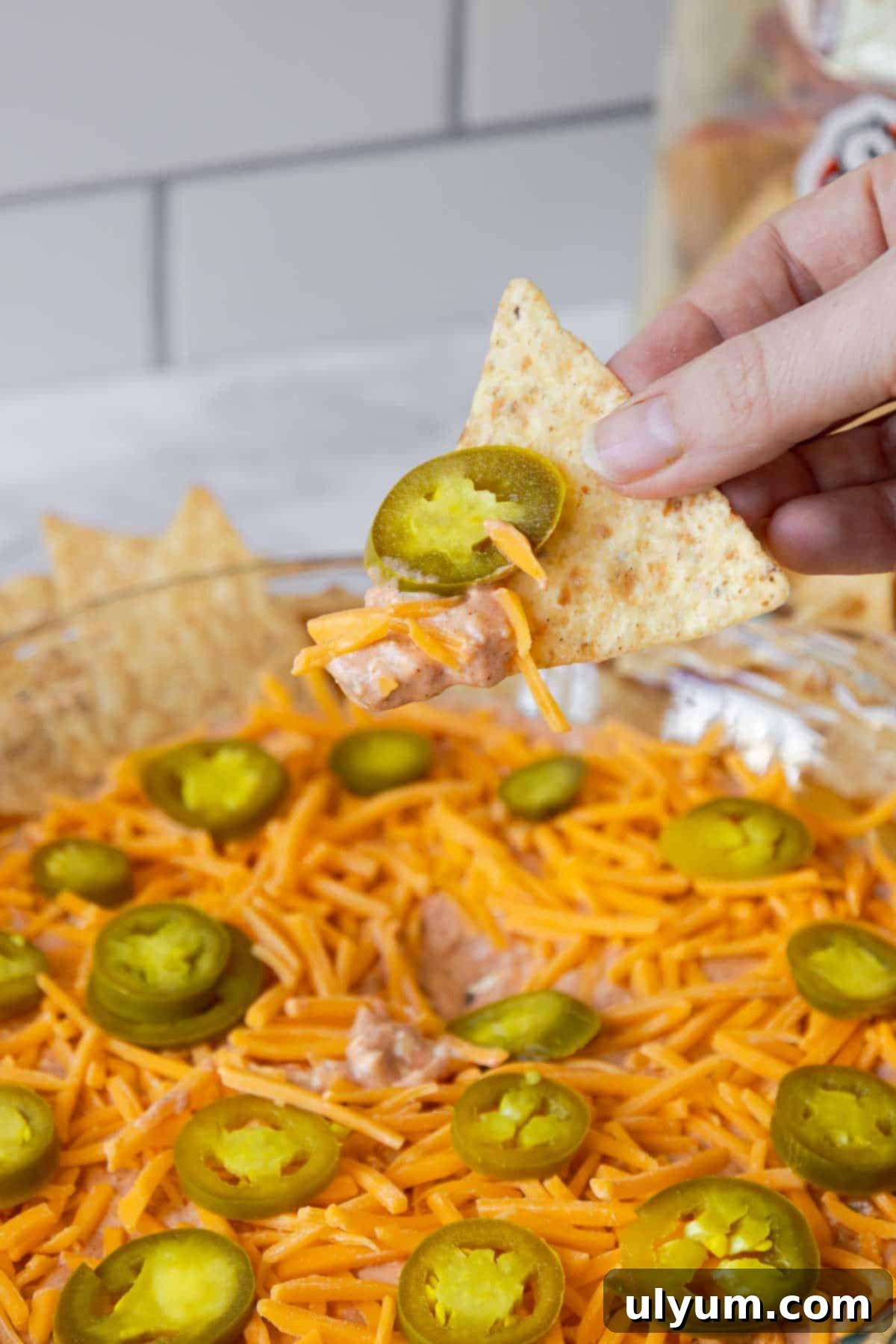 Hand scooping cream cheese salsa dip with melted cheese and jalapeño on a tortilla chip.