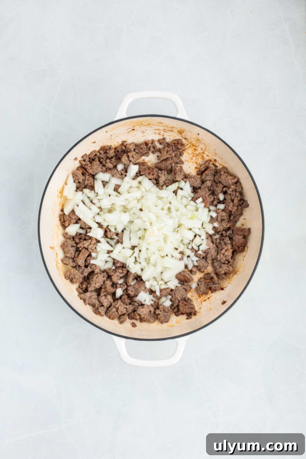 Overhead view of browned ground beef in a Dutch oven topped with chopped white onions.