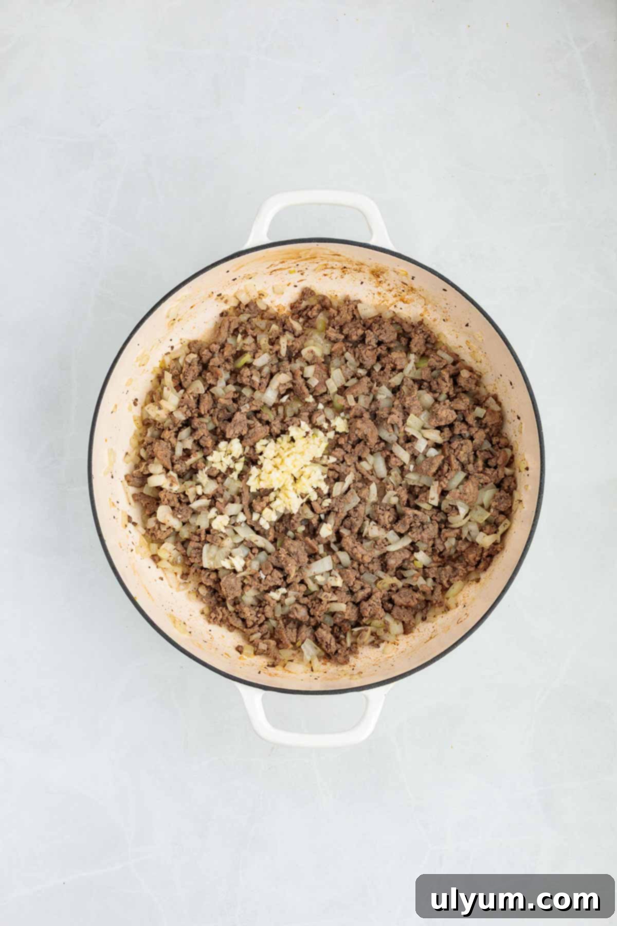 Cooked ground beef and onions in a Dutch oven with minced garlic added on top.