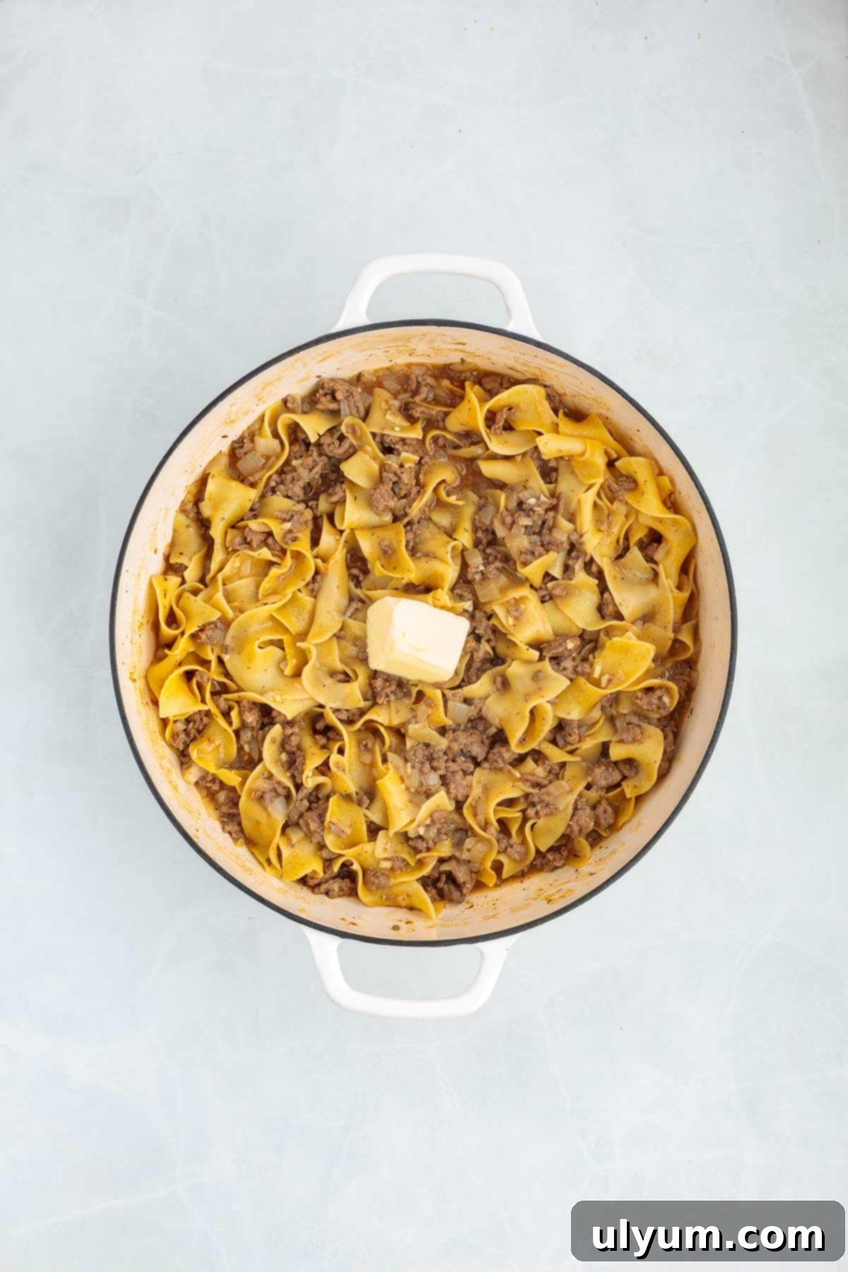 Butter melting on top of hot ground beef egg noodles in a Dutch oven.